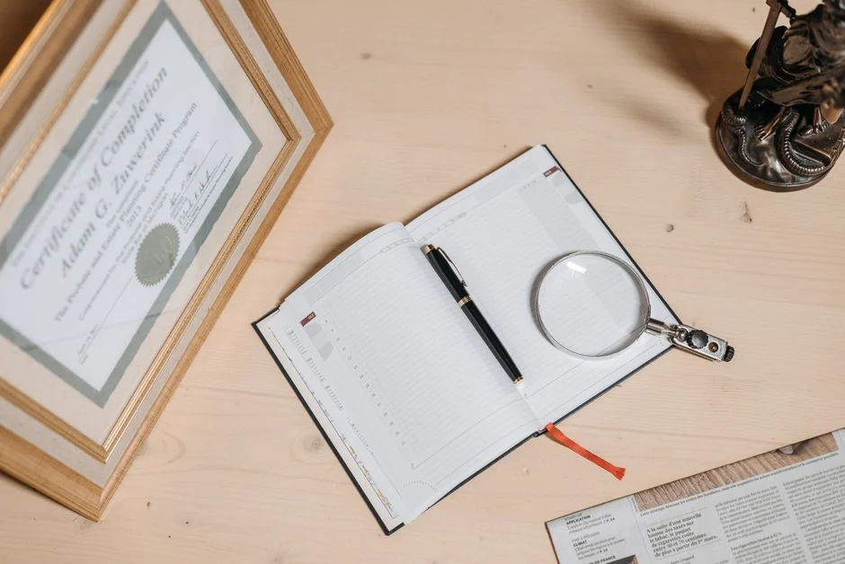 A tidy workspace featuring a certificate, open journal, magnifier, and statue on a wooden desk. - 人工智能领域专利布局指引a complete guide