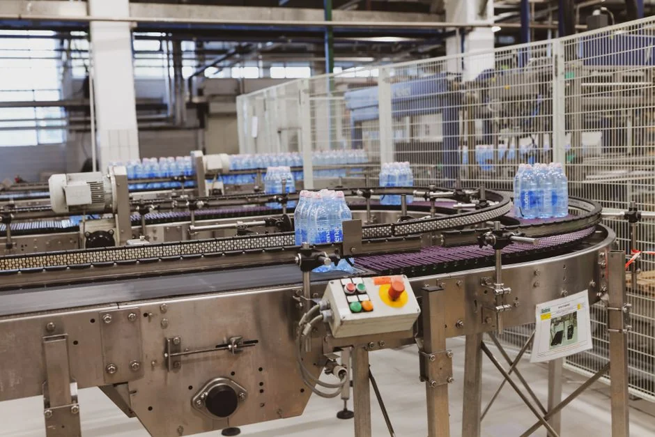Water bottles being processed on an automated conveyor in a modern factory setting. - 广州包装材料机械设备研发企业怎么构建专利壁垒防止竞品抄袭packaging machinery